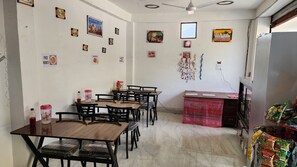 A dining area with multiple tables and chairs, a refrigerator stocked with food, and various wall decorations including framed pictures and a 'Happy Birthday' banner. - Hatu View Homestay (Kumharsain)