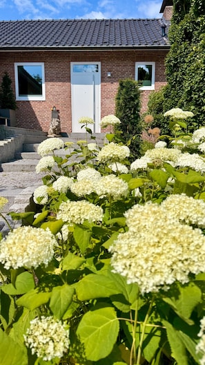 Ein Backsteinhaus mit Ziegeldach, einer Statue und einem Garten mit weißen Blumen.