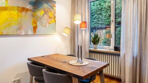 Un comedor con una mesa de madera, dos sillas, una lámpara de pie moderna y un ventanal con cortinas.