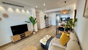 A modern living room with a flat-screen TV, a sofa, a coffee table, and a dining area with chairs and a table.