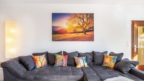 Un canapé modulable agrémenté de coussins colorés, un tableau représentant un arbre accroché au mur et une porte sur la droite.