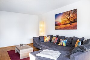 Una sala de estar moderna con un sofá gris, almohadones coloridos, una mesa de centro de madera y un cuadro de un árbol en la pared.
