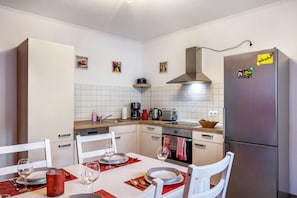 Una cocina moderna con armarios blancos, un refrigerador de acero inoxidable, un horno empotrado y una cafetera.