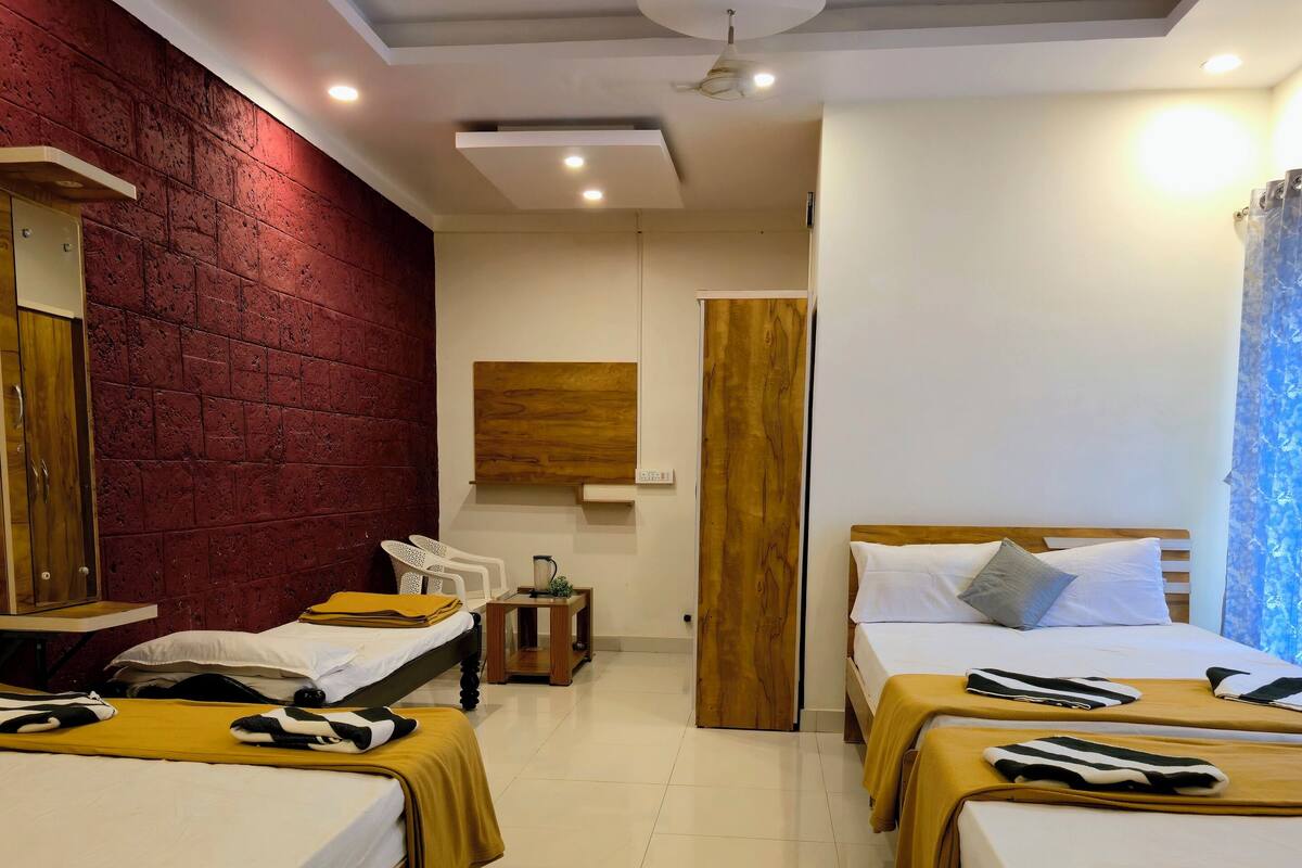 Een hotelkamer met twee bedden, een houten garderobe, een rode bakstenen muur en een plafondventilator.