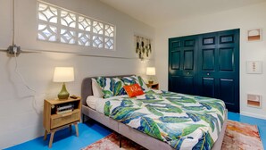 A bedroom with a bed, two bedside tables with lamps, a decorative wall hanging, a blue door, and a white wall with a window. - Simple Modern Gem 2 Blocks to Beach Pet Friendly (Indian Rocks Beach)