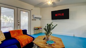 A living room with a blue couch, a wooden coffee table, a plant, and a TV displaying the Netflix logo. - Simple Modern Gem 2 Blocks to Beach Pet Friendly (Indian Rocks Beach)