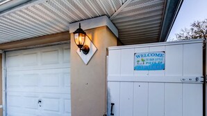 A garage door with a welcome sign, a wall-mounted light fixture, and a closed garage door. - Simple Modern Gem 2 Blocks to Beach Pet Friendly (Indian Rocks Beach)