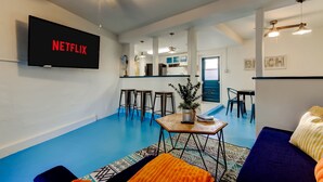 A modern living room with a flat-screen TV mounted on the wall, a ceiling fan, and a blue floor. - Simple Modern Gem 2 Blocks to Beach Pet Friendly (Indian Rocks Beach)