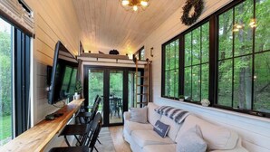 A cozy interior with a wooden ceiling, a sofa with a cushion, a TV on a wooden table, and large windows offering a view of the outdoors. - Hidden Retreat 4-homes 134 Acres (Nassau)