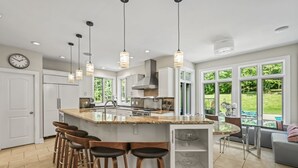 A modern kitchen with a large island, bar stools, pendant lighting, and a view of the garden. - Hidden Retreat 4-homes 134 Acres (Nassau)