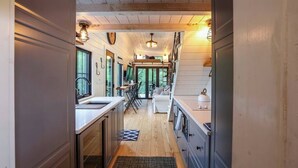 A narrow hallway with wooden floors and walls, leading to a dining area with a table and chairs. There is a kitchen area with cabinets and a sink on the left. - Hidden Retreat 4-homes 134 Acres (Nassau)