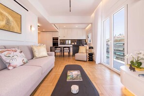 A modern living room with a sofa, a coffee table, and a view of the city through large windows. - Michalakopoulou Corner & Bright Apartment, Luxury (Athens)