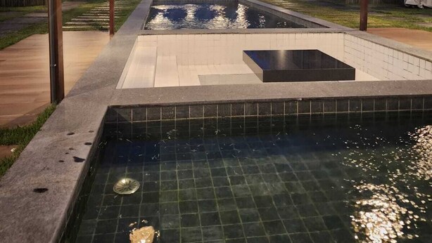 Une piscine surmontée d’une pergola, entourée d’une clôture en bois et avec un bâtiment visible au fond.