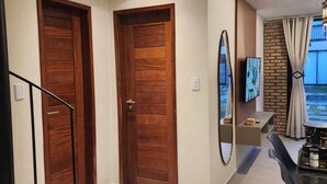 Un intérieur moderne avec deux portes en bois, un escalier, un coin repas comprenant une table et des chaises, et un téléviseur fixé au mur.
