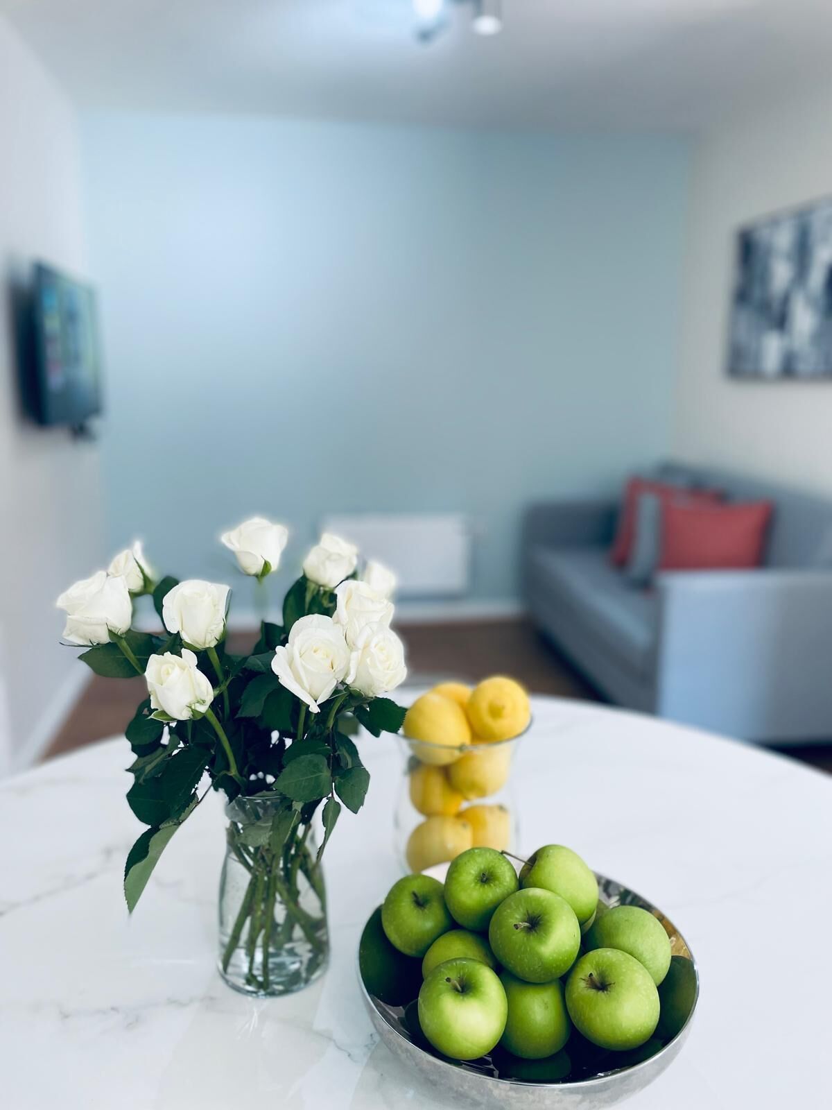 Une table à manger ornée d’un vase de roses blanches et d’un saladier de pommes vertes.