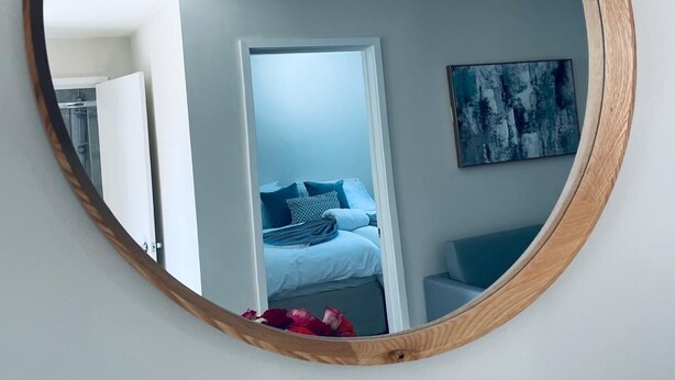 A round mirror with a wooden frame on a wall. - Ivy Cottage Two Bedroom & Garden in Temple Fortune (London)