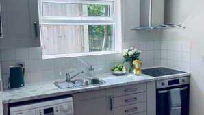 A compact kitchen with a built-in washing machine, a sink, and an oven. - Ivy Cottage Two Bedroom & Garden in Temple Fortune (London)
