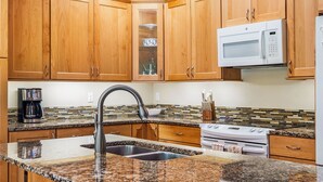 Una cocina con armarios de madera, encimera de granito, pileta de acero inoxidable, microondas y estufa.