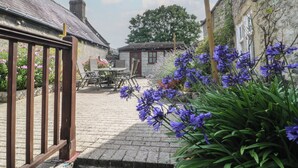 A courtyard with a stone building, a wooden fence, and a table with chairs.