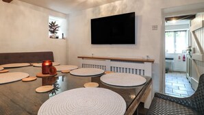 A dining area with a wooden table, woven placemats, a red mug, and a television mounted on the wall.