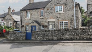 A stone building with a blue door, multiple windows, and a stone wall in front.