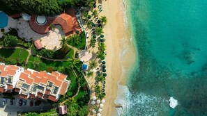 Luchtbeeld van een kusthotel met strand, palmbomen en een zwembad.
