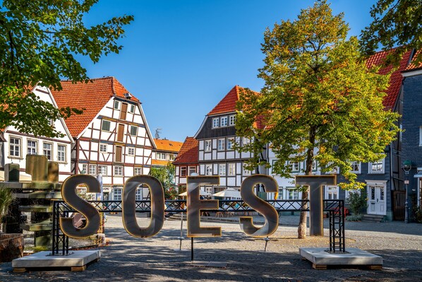 A historic town square with traditional half-timbered houses, a fountain, and the word "SOEST" prominently displayed in the foreground.