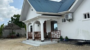 A white building with a covered porch, a metal roof, and a small air conditioning unit mounted on the wall.