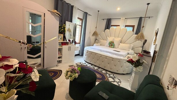A modern living room with a tufted sofa, a round coffee table, and a green ottoman. There is a white armchair and a small table with a vase of flowers.