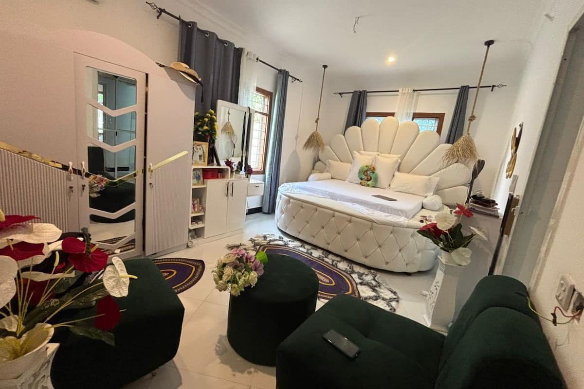 A modern living room with a tufted sofa, a round coffee table, and a green ottoman. There is a white armchair and a small table with a vase of flowers.