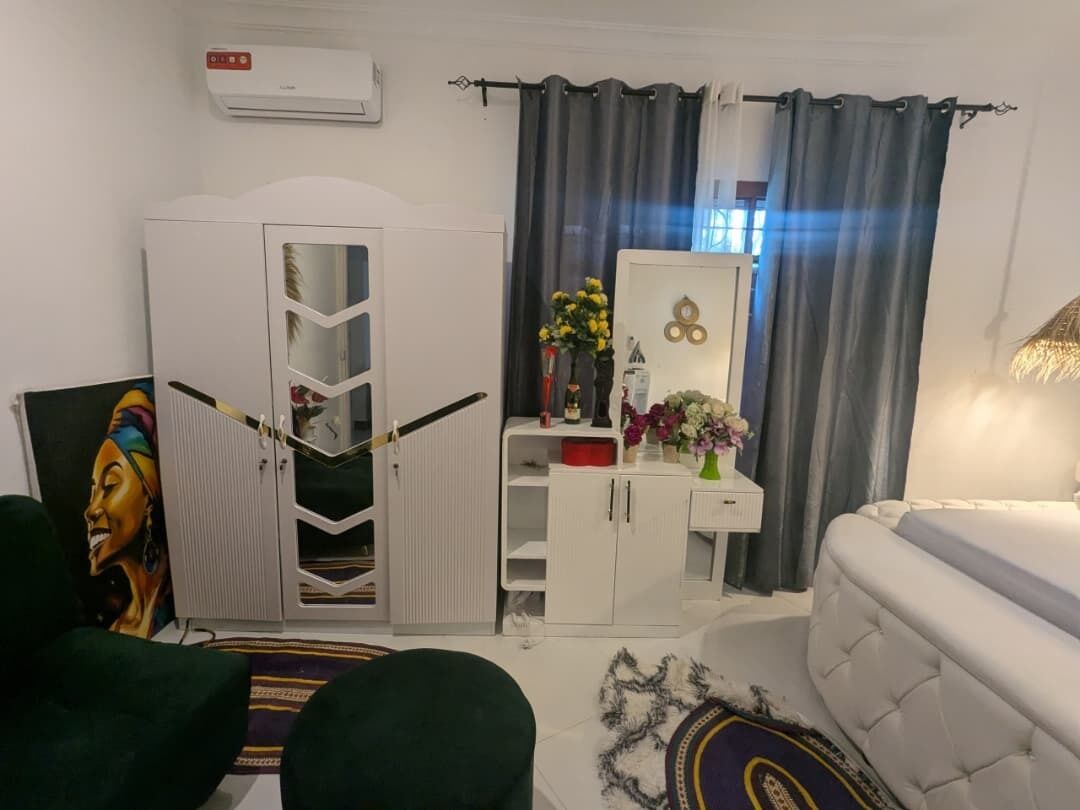 A bedroom with a bed, a wardrobe, a desk with a mirror, and a painting on the wall.