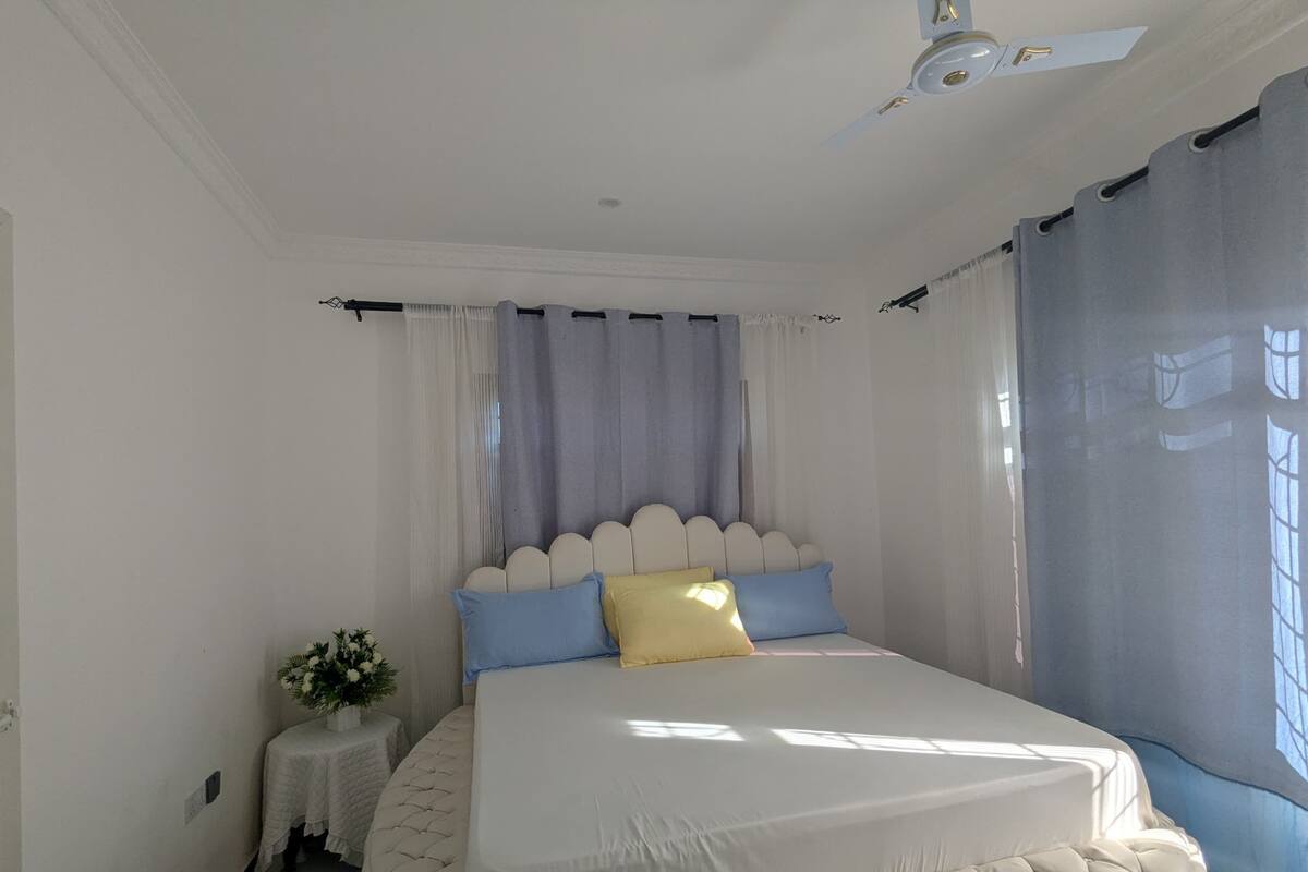 A bedroom with a large bed, a small bedside table, and a window with curtains.