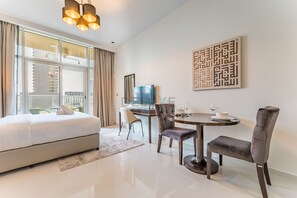 A modern hotel room with a large bed, a dining table with chairs, a TV, and a large window with curtains. - Near Circle Mall, Park, Jogging Track, Bus Stop And Grocery Stores (Dubai)