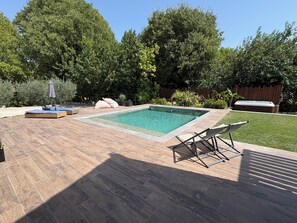 Ein rechteckiger Pool mit einer gefliesten Liegefläche, Liegestühlen und einem Whirlpool.