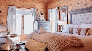 A cozy log cabin bedroom with a large bed, a chair, and a dresser. - Mirror Lake - Rare private lake! (Scales Mound)
