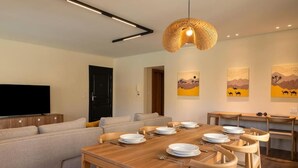 A modern dining area with a wooden table set for six, a sofa, and a television in the background. - Kennah Milena | Stone Residence, New Cairo - Families Only (New Cairo)
