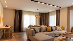 A modern living room with a sectional sofa, a coffee table, and a dining area with a wooden table and chairs. - Kennah Milena | Stone Residence, New Cairo - Families Only (New Cairo)