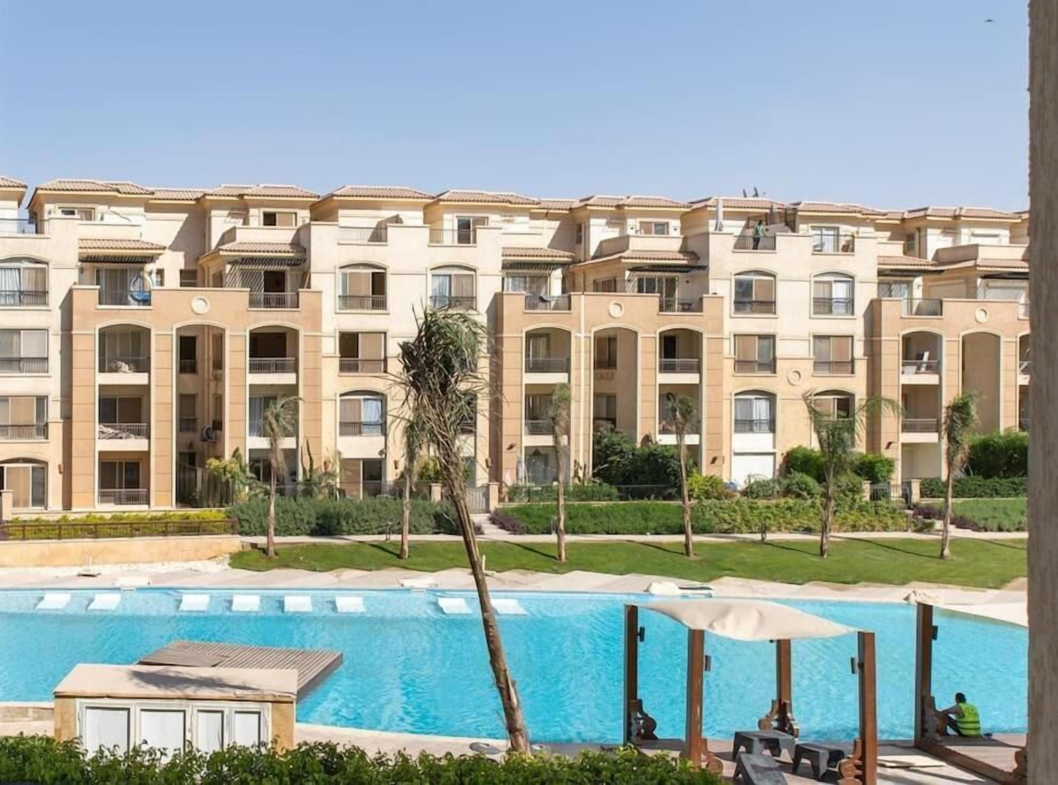 A multi-story hotel with a swimming pool, outdoor seating, and palm trees.