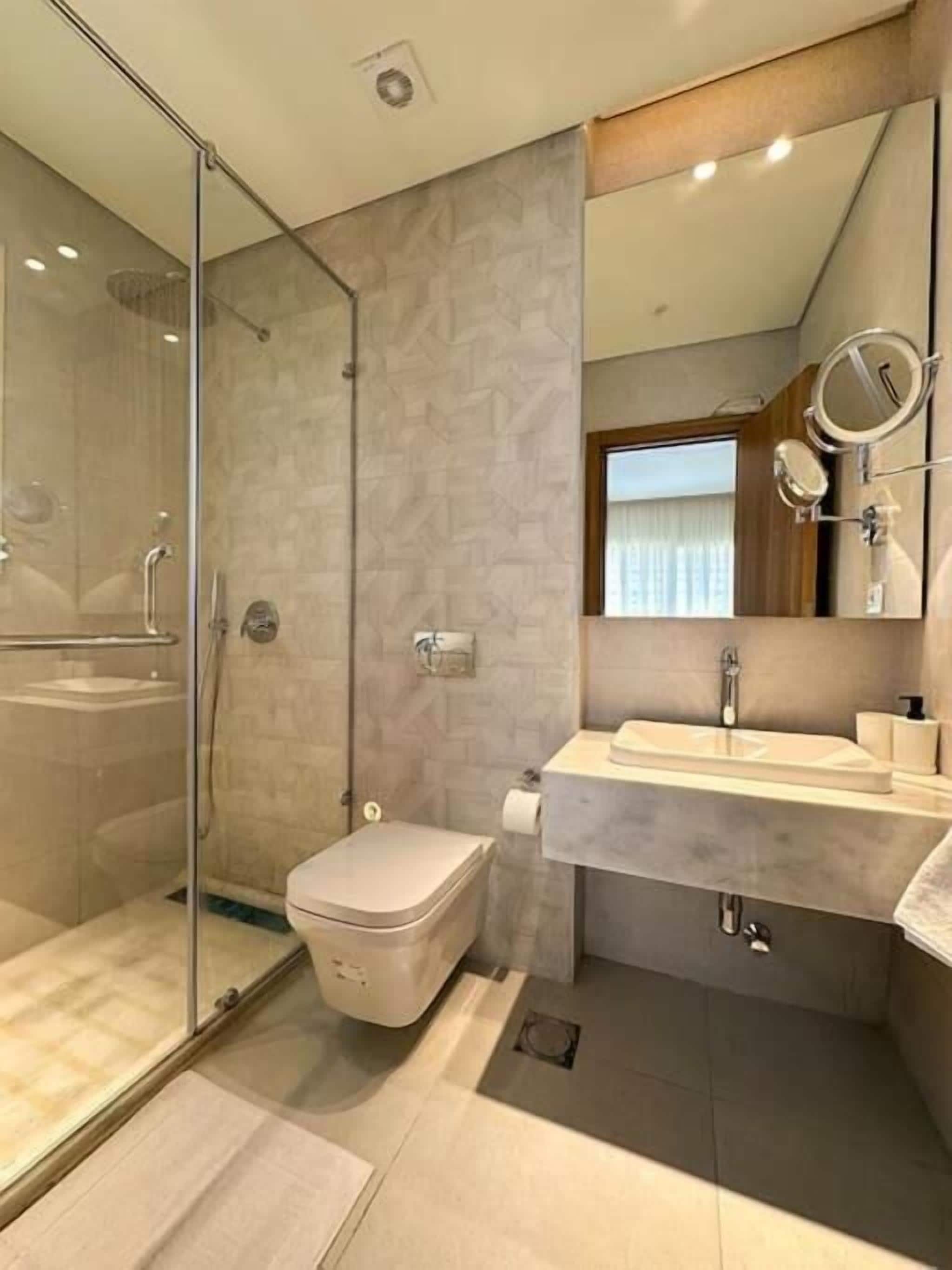 A modern bathroom with a glass shower enclosure, a toilet, a vanity with a mirror, and a sink.