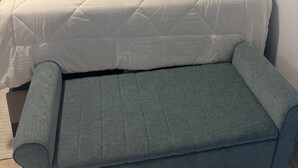 Ein ordentlich bezogenes Bett mit weißer Decke, einem grauen Kopfteil und einer grauen Bank am Fußende.
