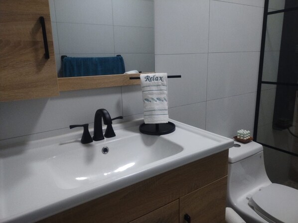 A bathroom with a white sink, black faucet, and a toilet. A towel rack with a towel is mounted above the sink.