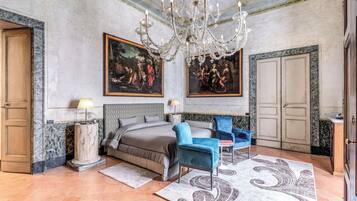 A spacious bedroom with a large bed, a chandelier, and two paintings on the wall.