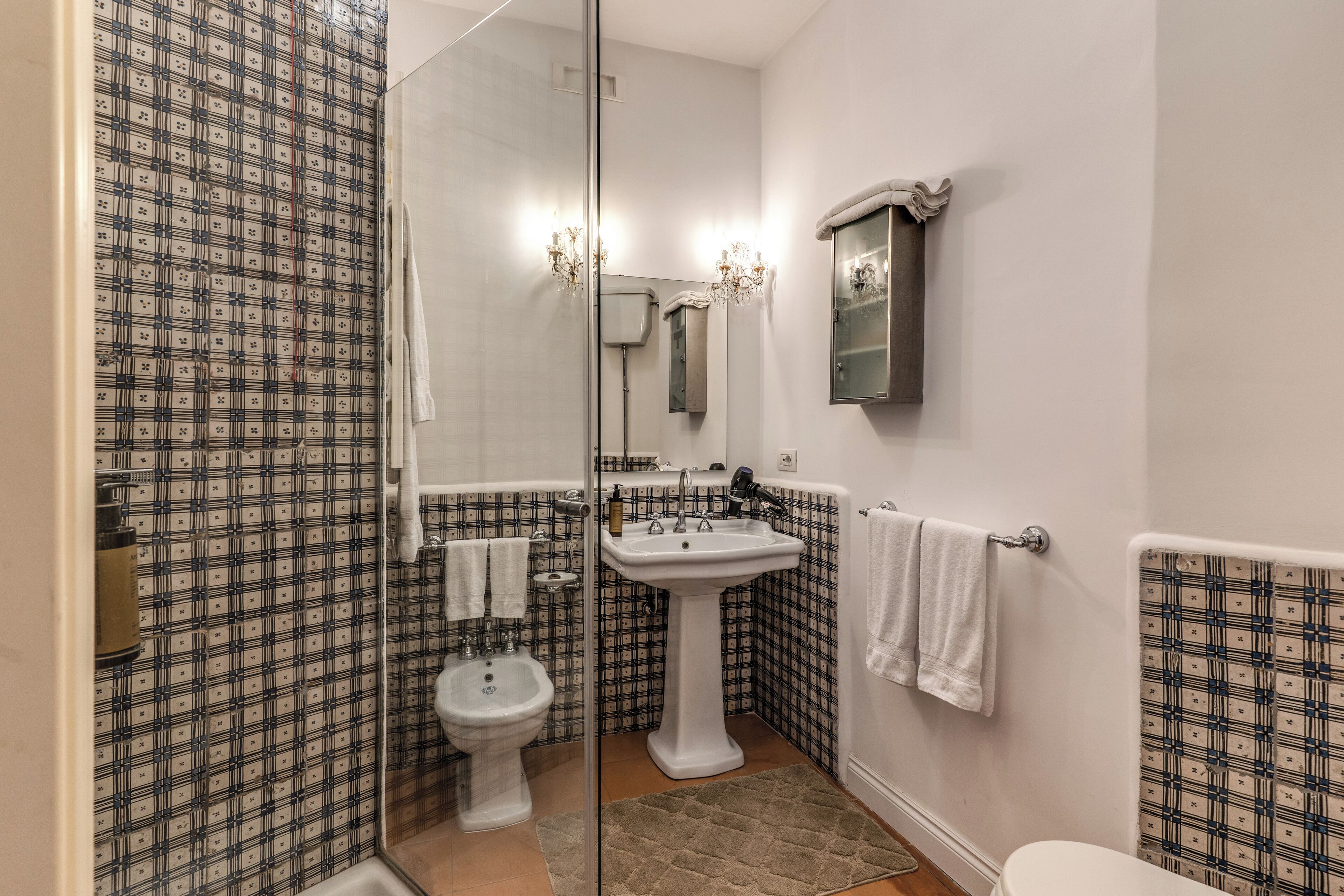 Une salle de bain avec un mur recouvert de carreaux décoratifs, un lavabo sur pied, un bidet et des toilettes.