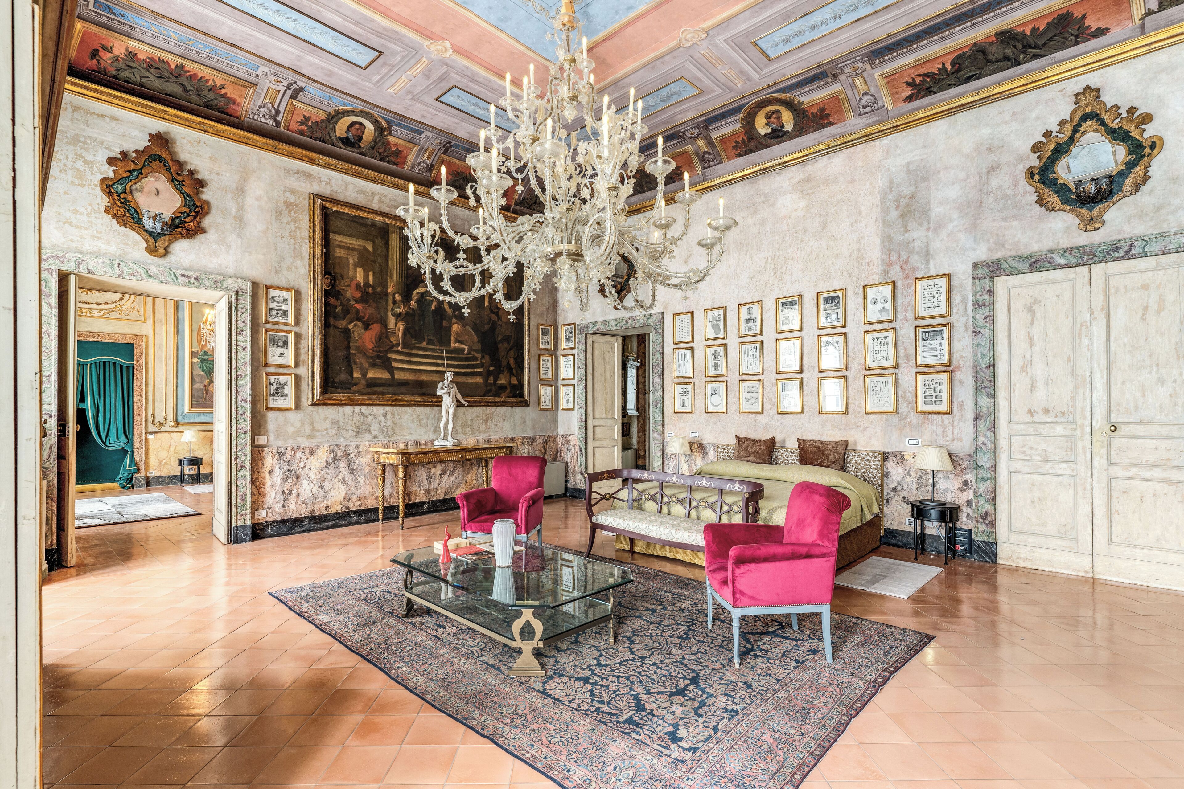 A luxurious room with a large chandelier, a grand painting, and a collection of framed pictures on the wall.