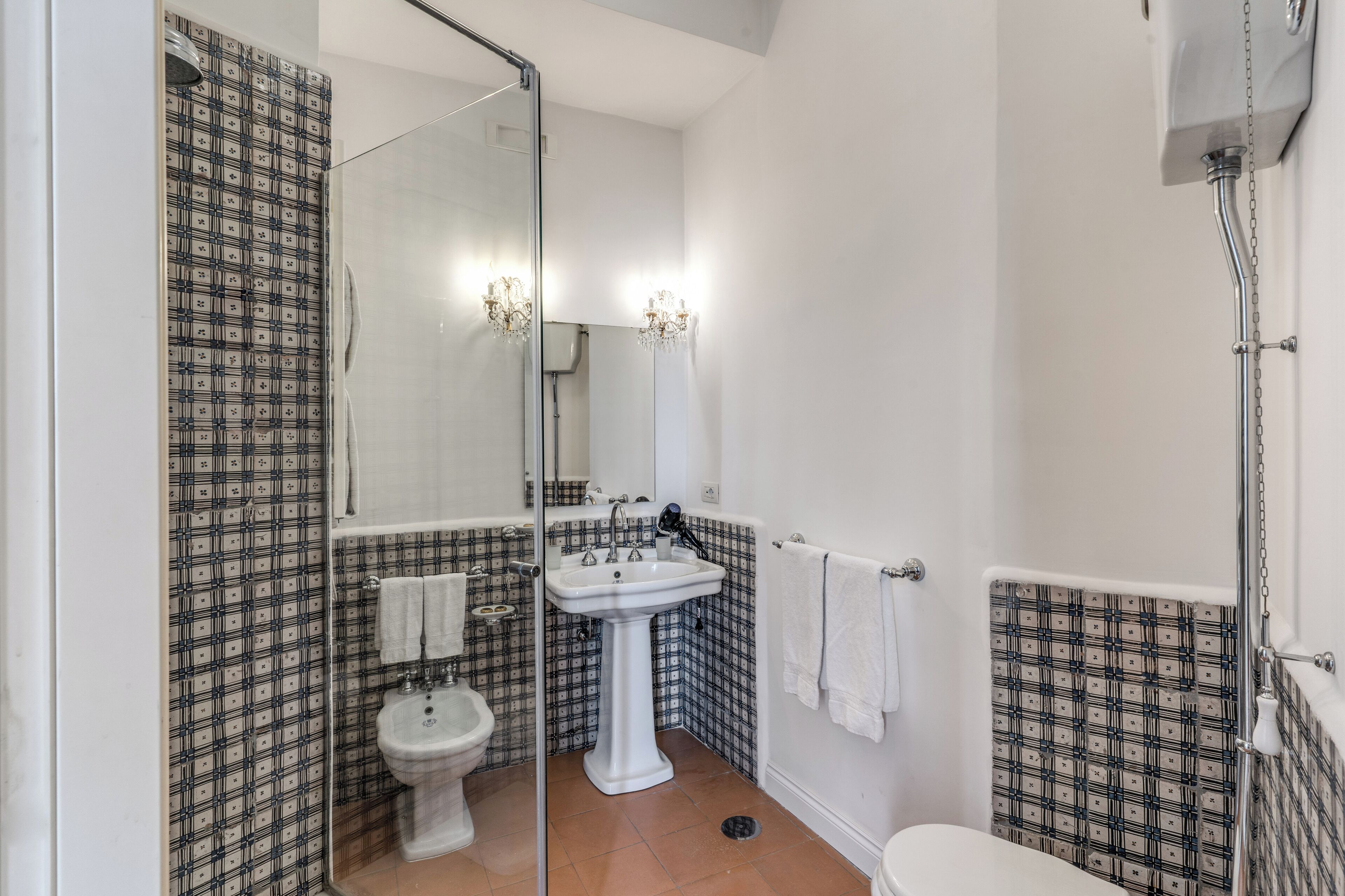 A bathroom with a pedestal sink, a toilet, a shower, and patterned walls.