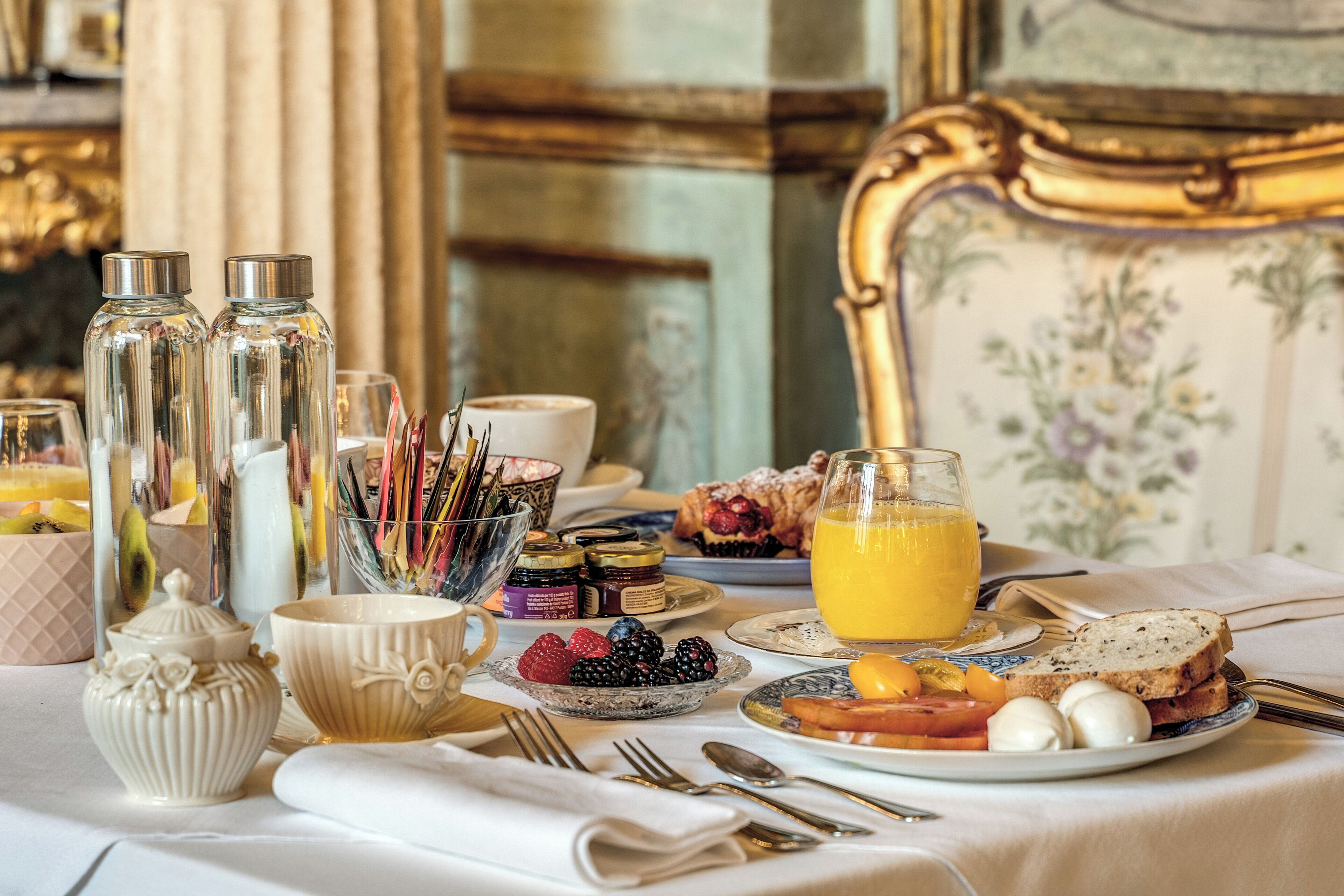 Una tavola imbandita per la colazione, con diversi cibi, utensili e oggetti decorativi.