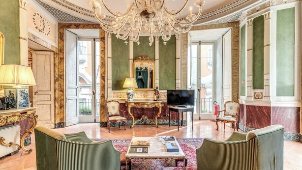 A luxurious living room with a chandelier, green upholstered chairs, a coffee table, and a television. - Palazzo Doria Suites (Naples)
