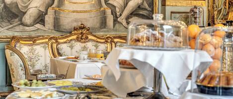 A luxurious dining area with a marble table set for breakfast, featuring an array of pastries, fruits, and a coffee station.