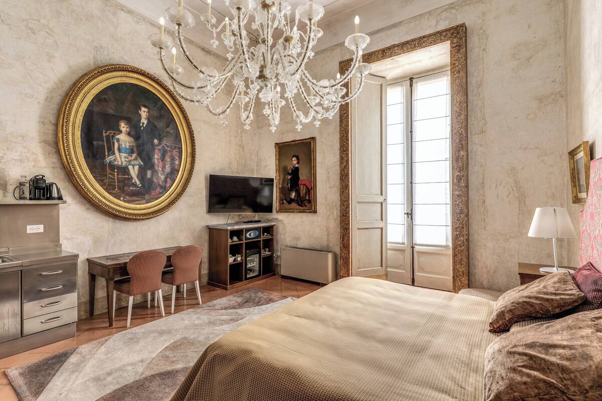 A bedroom with a large bed, a TV, a desk, and a chandelier.