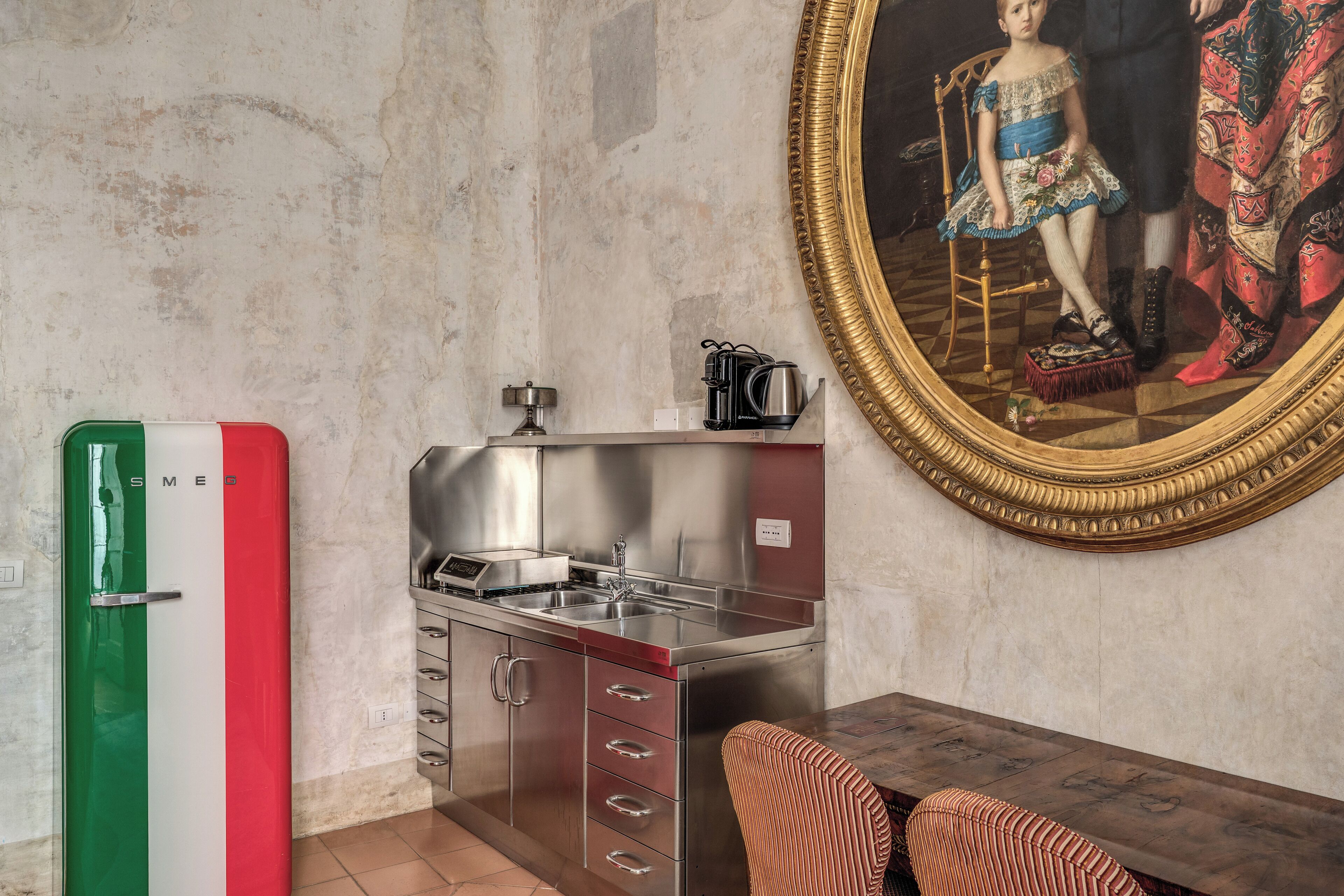 A compact kitchen with a sink, stove, and cabinets, a small dining table with chairs, and a framed painting on the wall.